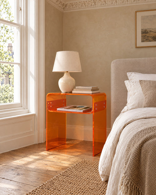 Amber acrylic bedside table beside a linen bed in a British bedroom with a sash window