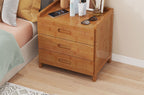 Honey bamboo bedside table with three drawers beside a bed