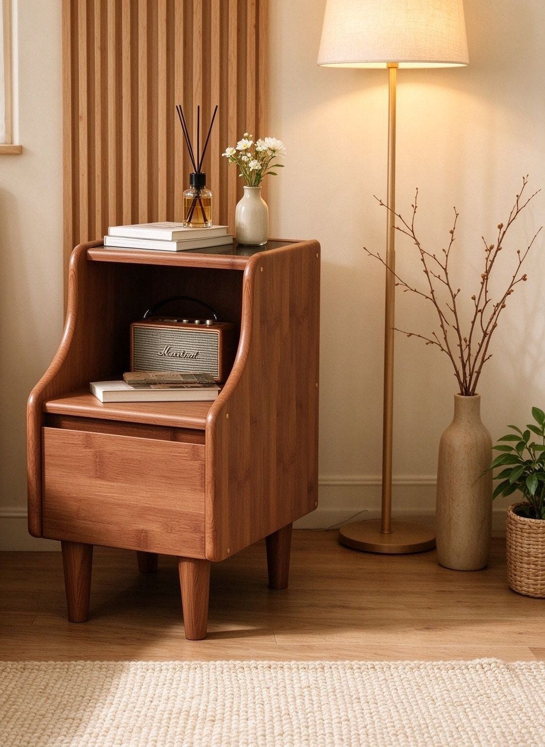 Front view of the walnut-tone bamboo bedside cabinet with curved sides, black top, open shelf and drawer