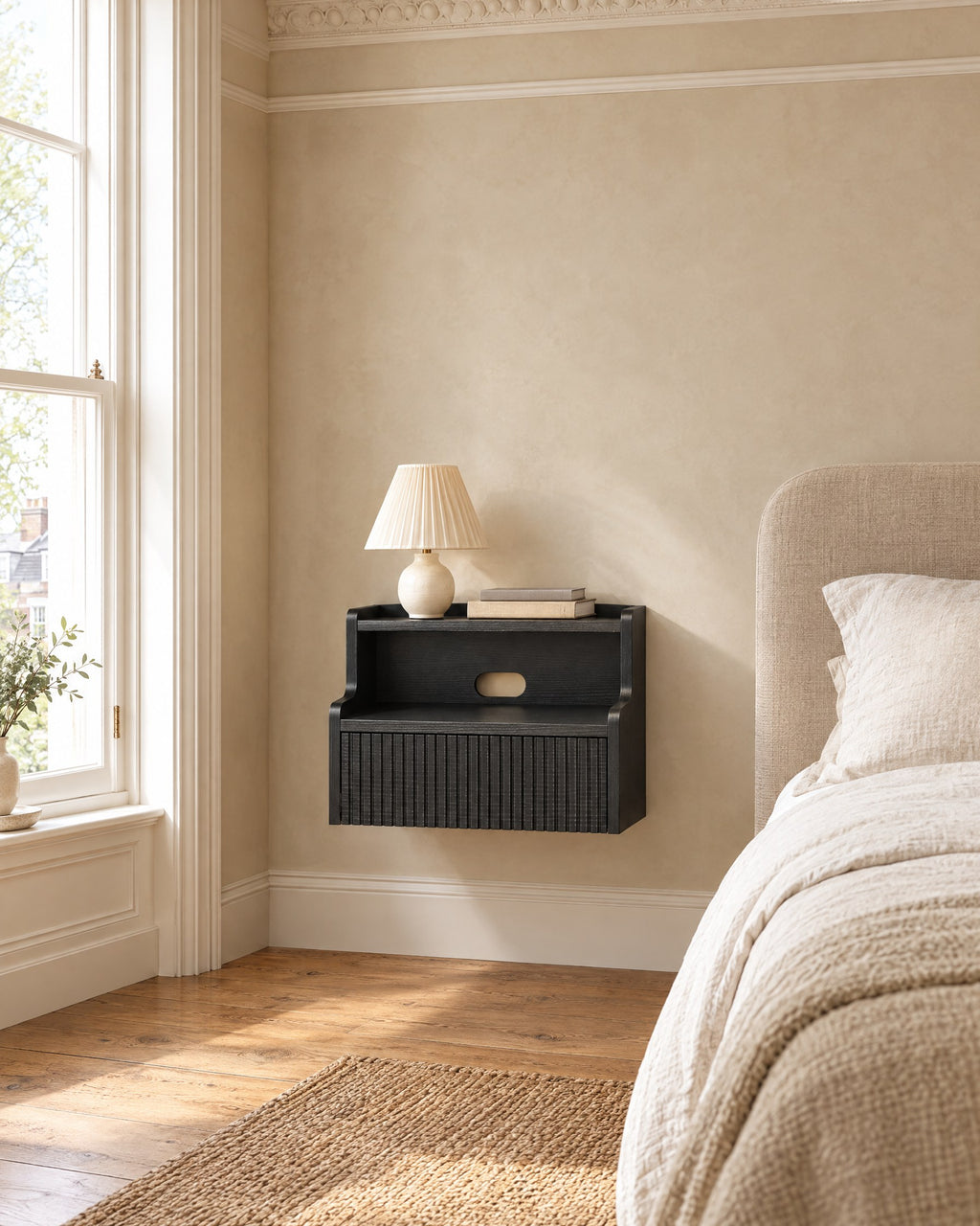Black floating bedside table beside a linen bed in a bright British bedroom with a sash window