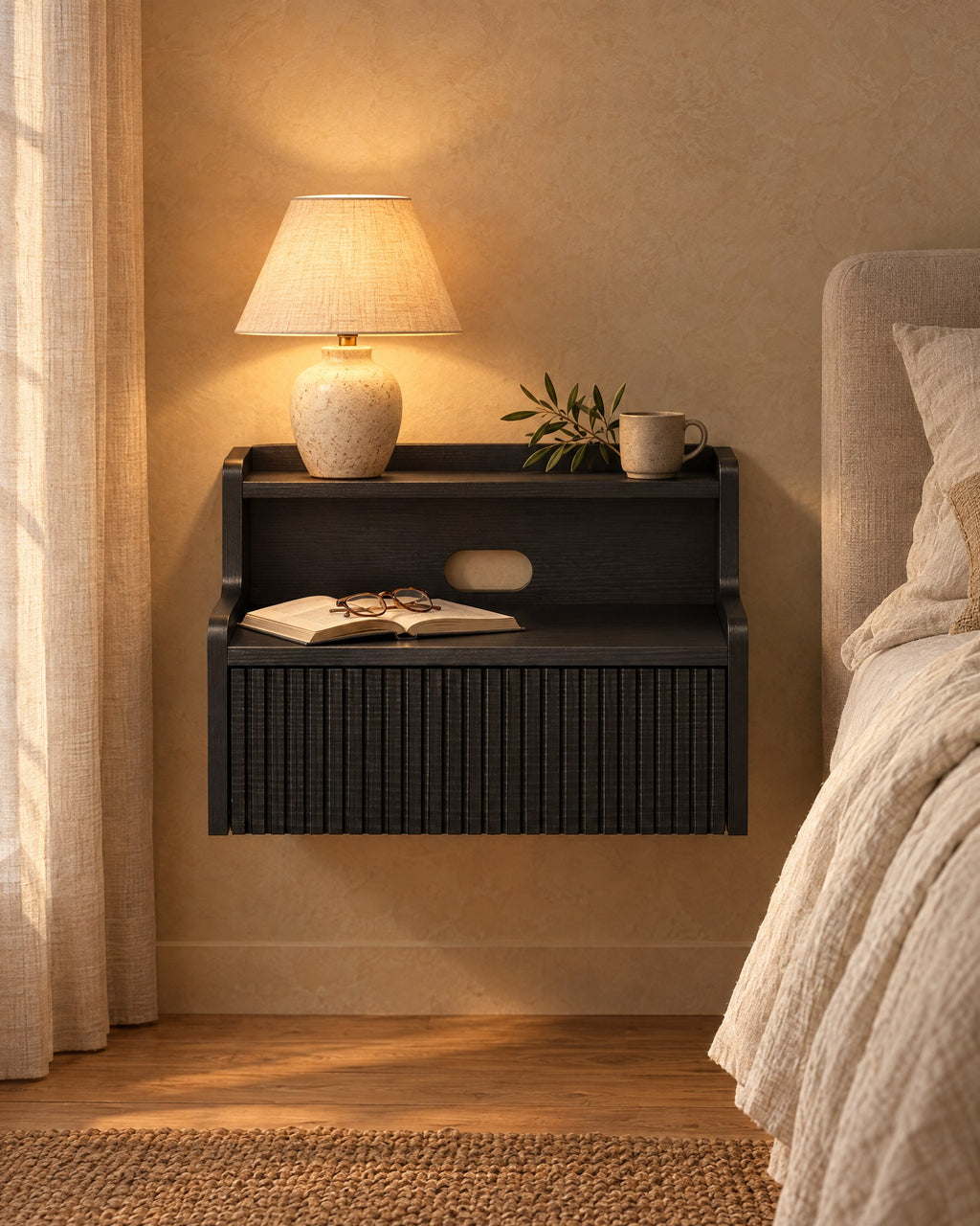Black floating bedside table with a lamp switched on and an open book in the evening