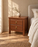 Three-quarter view of the brown wood bedside table with two drawers and brass pulls