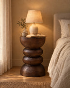 Carved wood pedestal bedside table, lamp switched on and an open book in the evening