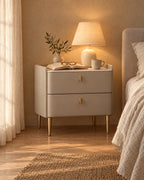 Champagne grey bedside table with gold legs, a lamp switched on and an open book in the evening
