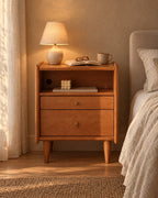 Cherry wood bedside table with open niche with a lamp switched on and an open book in the evening