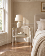 Clear acrylic bedside table beside a linen bed in a British bedroom with a sash window