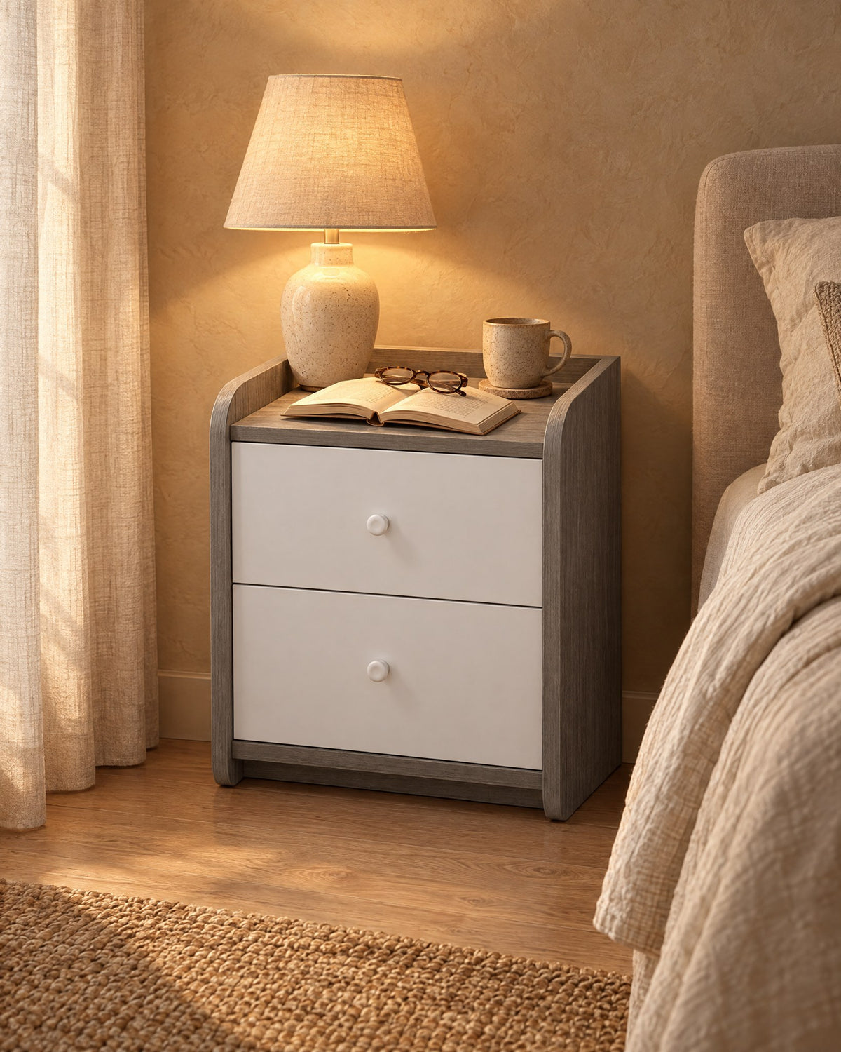 Compact grey and white bedside table with a lamp switched on and an open book in the evening