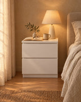Compact white bedside table with a lamp switched on and an open book in the evening