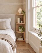Corner bedside shelf with four rounded tiers beside a linen bed in a British bedroom with a sash window
