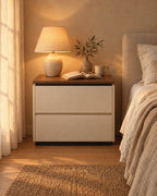 Cream bedside table with a walnut-tone top, a lamp switched on and an open book in the evening