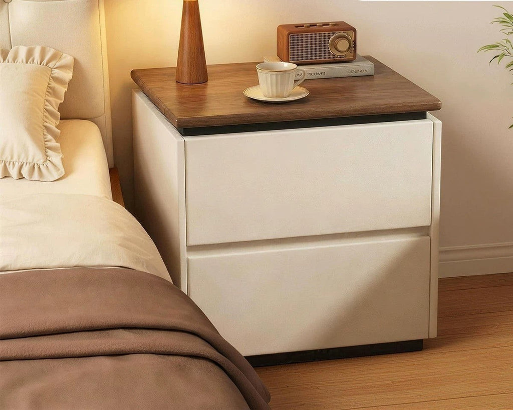Cream bedside table with two drawers and a walnut-tone top beside a bed