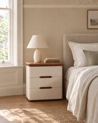 Cream three-drawer bedside table beside a linen bed in a British bedroom with a sash window