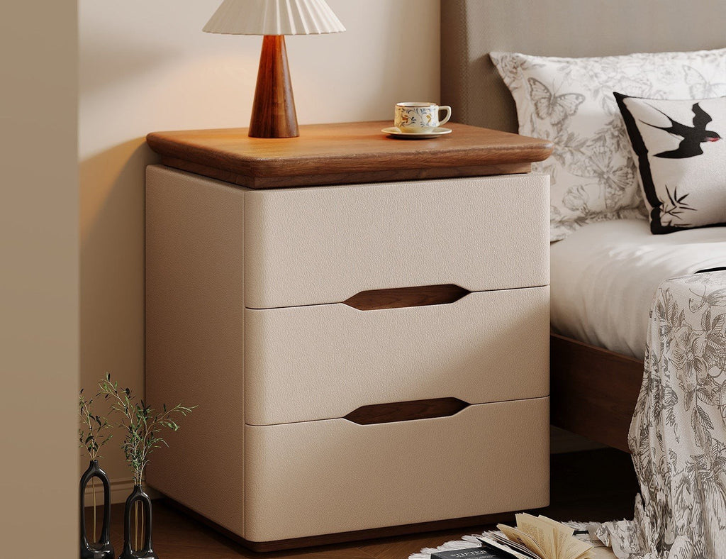 Cream bedside table with three drawers and a walnut-tone top beside a bed
