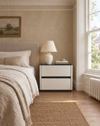 Cream bedside table with a glossy black top and two drawers beside a linen bed in a British bedroom with a sash window