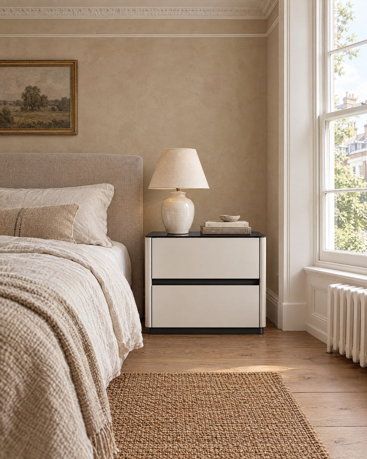 Cream bedside table with a glossy black top and two drawers beside a linen bed in a British bedroom with a sash window