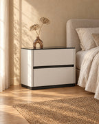 Three-quarter view of the cream bedside table with a glossy black top and two drawers