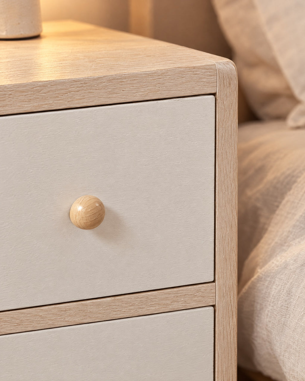Close-up of the round light-wood knob on the white drawer of the cream bedside table