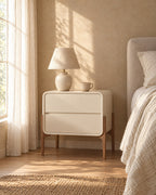 Cream bedside table on walnut-tone legs with a ceramic lamp in morning light