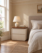 Cream bedside table with a walnut-tone top and two drawers beside a linen bed in a British bedroom with a sash window