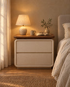 Cream bedside table with a walnut-tone top and two drawers with a lamp switched on, a book and reading glasses in the evening