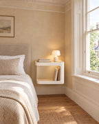 Cream floating bedside table beside a linen bed in a bright British bedroom with a sash window