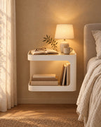 Cream floating bedside table with a lamp switched on and an open book in the evening