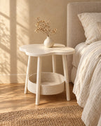 Three-quarter view of the cream flower-shaped bedside table with a storage basket beside a bed
