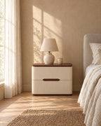 Cream leather-look bedside table with walnut-tone top with a ceramic lamp in morning light
