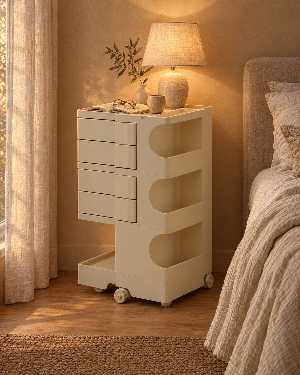 Cream rolling bedside trolley with swivel drawers, a lamp switched on and an open book in the evening