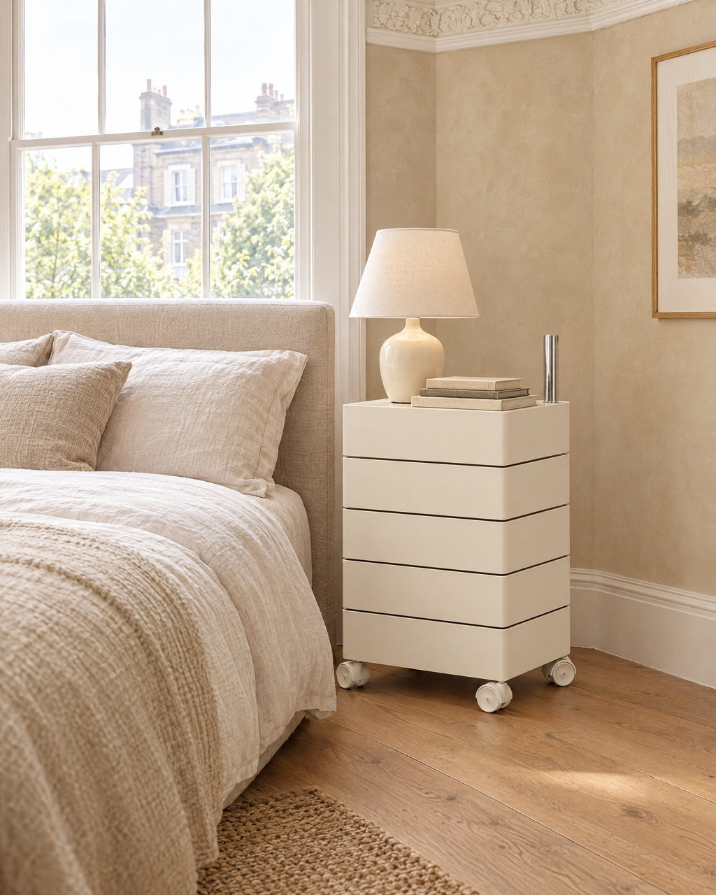 Cream rotating storage unit beside a linen bed in a bright British bedroom with a sash window