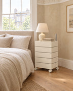 Cream rotating storage unit beside a linen bed in a bright British bedroom with a sash window