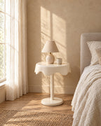 Cream round pedestal bedside table with a ceramic lamp in morning light