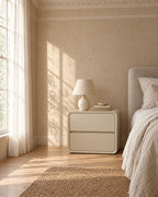Cream rounded cube bedside table beside a linen bed in a bright British bedroom with a sash window