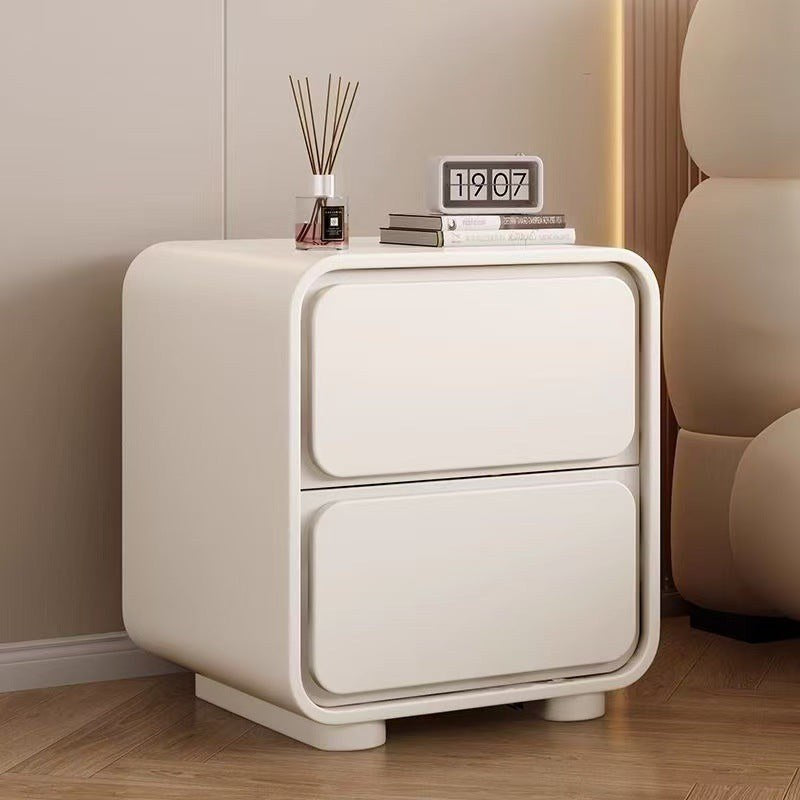 Cream bedside table with a rounded frame and two drawers beside a bed