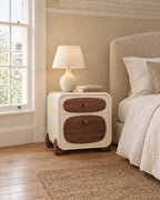Cream bedside table with walnut drawer fronts beside a linen bed in a British bedroom with a sash window
