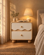 Cream wave bedside table with a lamp switched on, an open book and reading glasses in the evening