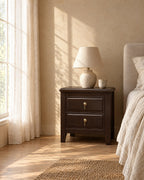 Dark wood bedside table with brass drop handles in warm morning light with window shadows on the wall