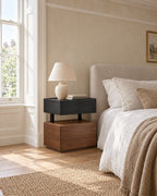 Black and walnut floating bedside table beside a linen bed in a British bedroom with a sash window