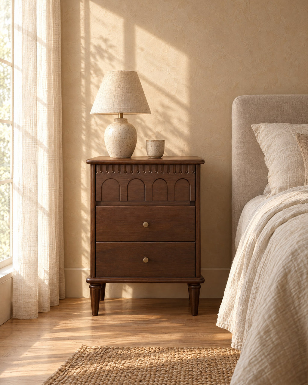 Dark walnut bedside table with carved arches in morning light