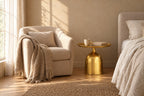 Gold metal round bedside table beside a linen armchair in a reading corner