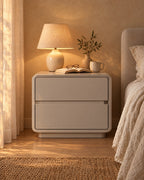 Greige lacquered bedside table with a lamp switched on and an open book in the evening