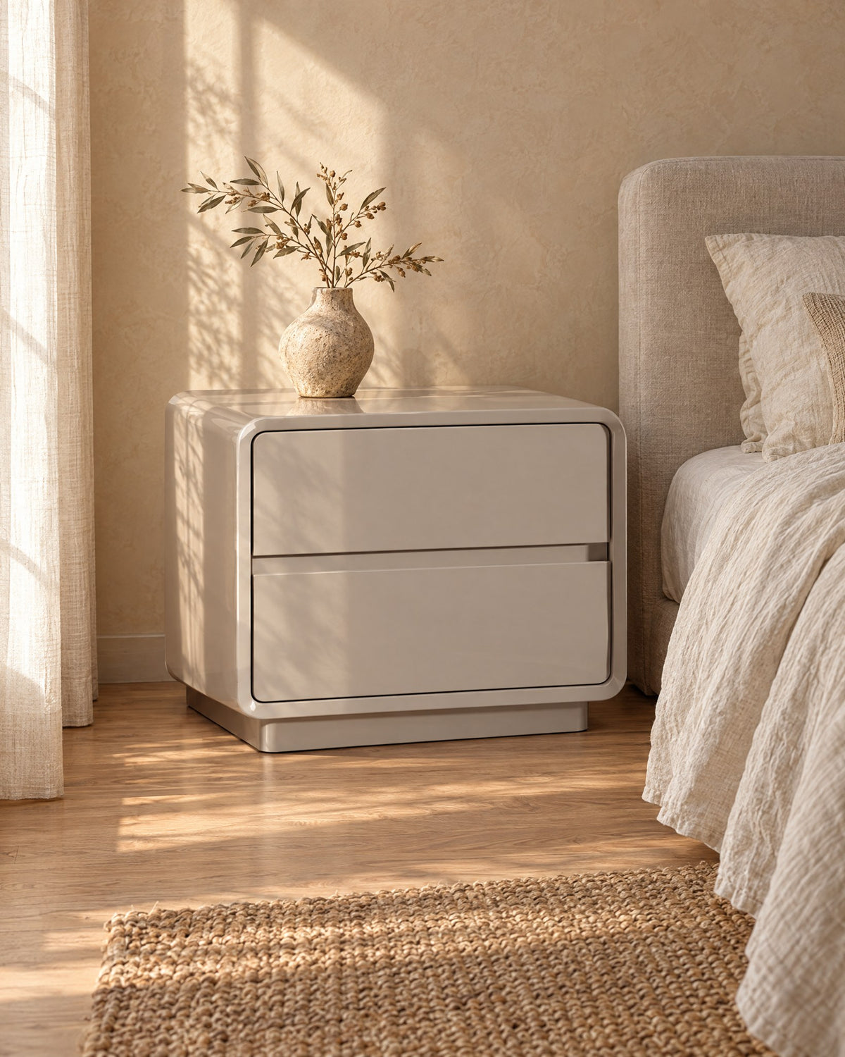 Three-quarter view of the greige lacquered bedside table showing its rounded frame