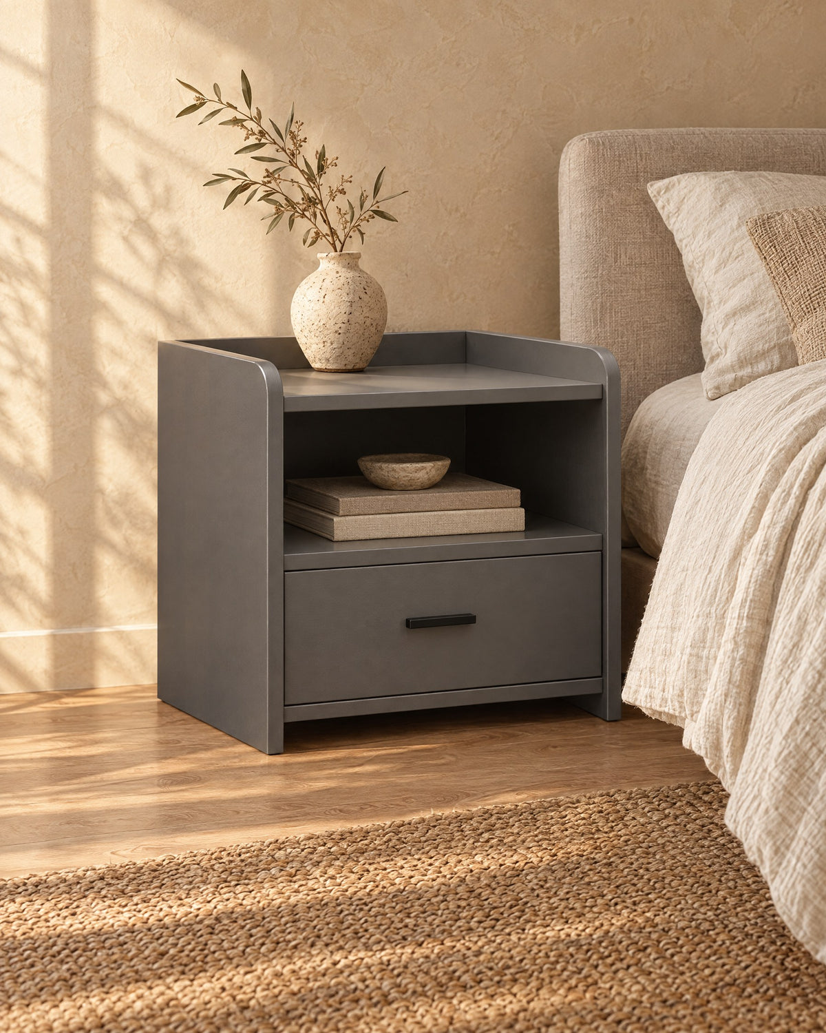 Three-quarter view of the grey bedside table with an open shelf and one drawer