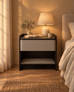 Grey and espresso bedside table with a lamp switched on and an open book in the evening