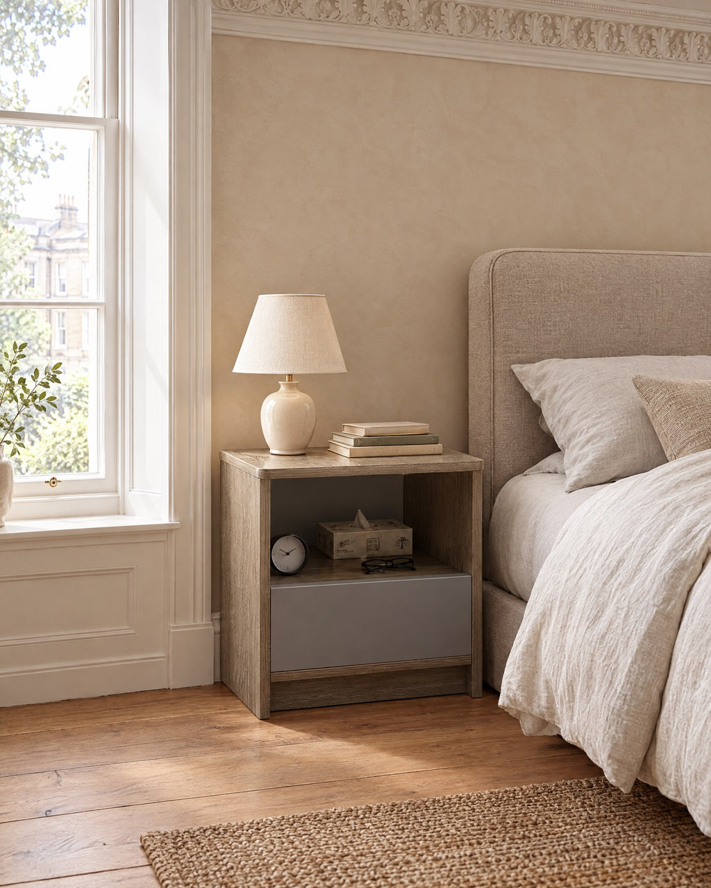 Grey oak bedside table beside a linen bed in a British bedroom with a sash window