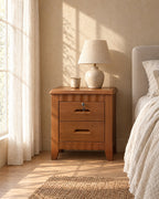 Lockable brown wooden bedside table with two drawers and scalloped rails with a ceramic lamp in morning light