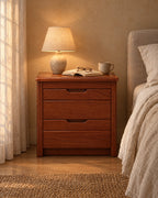 Mahogany-tone wood bedside table with 2 drawers with a lamp switched on and an open book in the evening