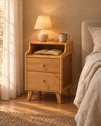 Narrow natural bamboo bedside table with an open niche, a lamp switched on and an open book in the evening