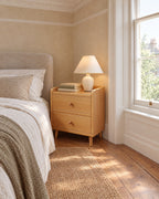 Narrow cherry bedside table beside a linen bed in a British bedroom with a sash window