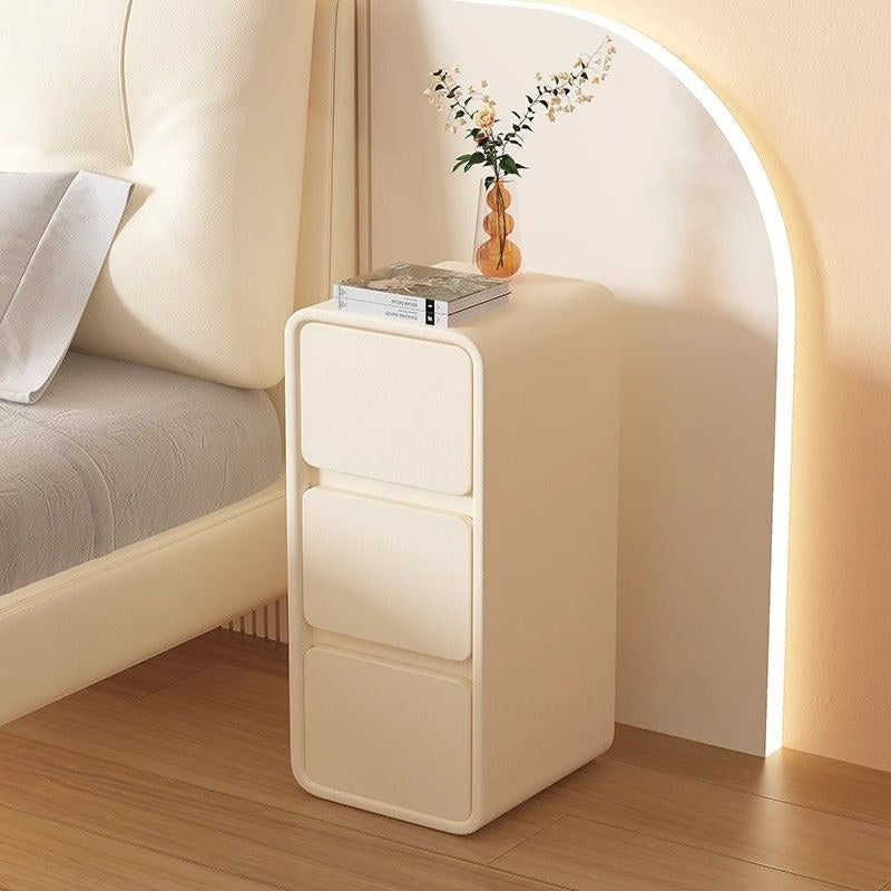 Narrow cream bedside table with three handle-free drawers, supplier photograph
